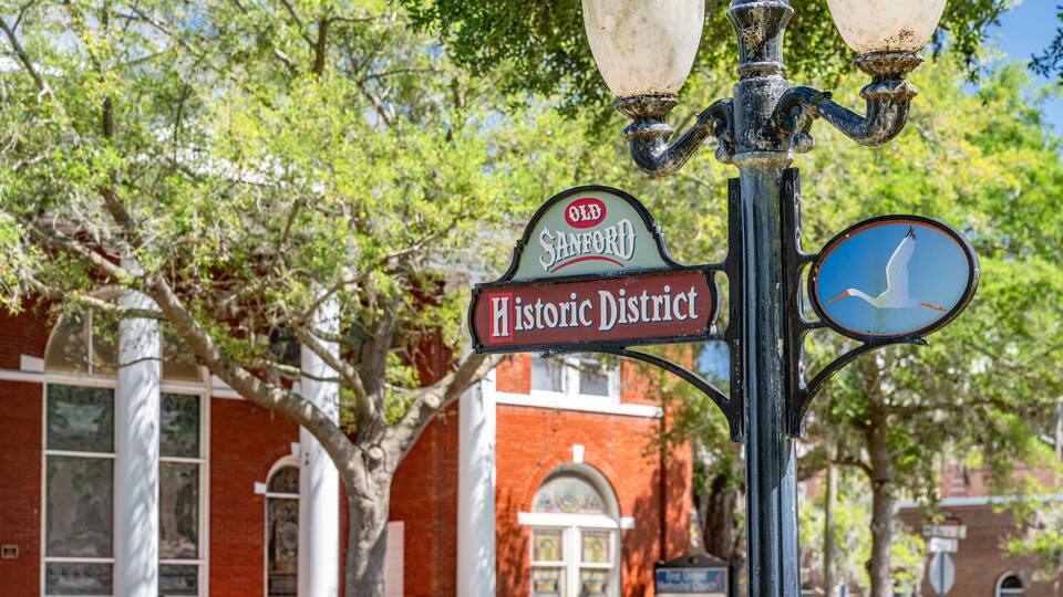 A historic district sign with a bird symbol, a lamp post, and a brick building with arched windows.