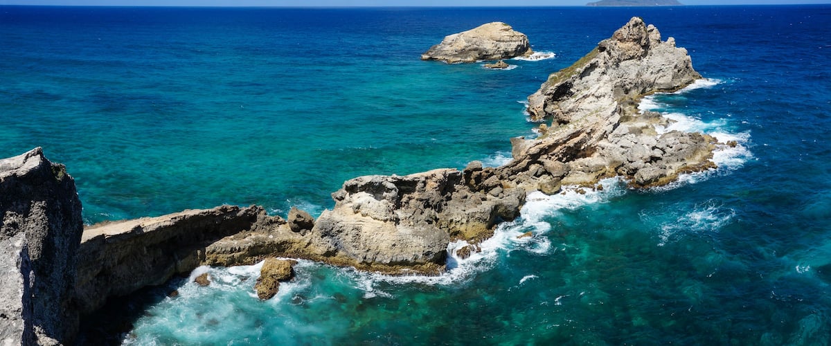 A rocky coastline with clear blue waters and a distant island.