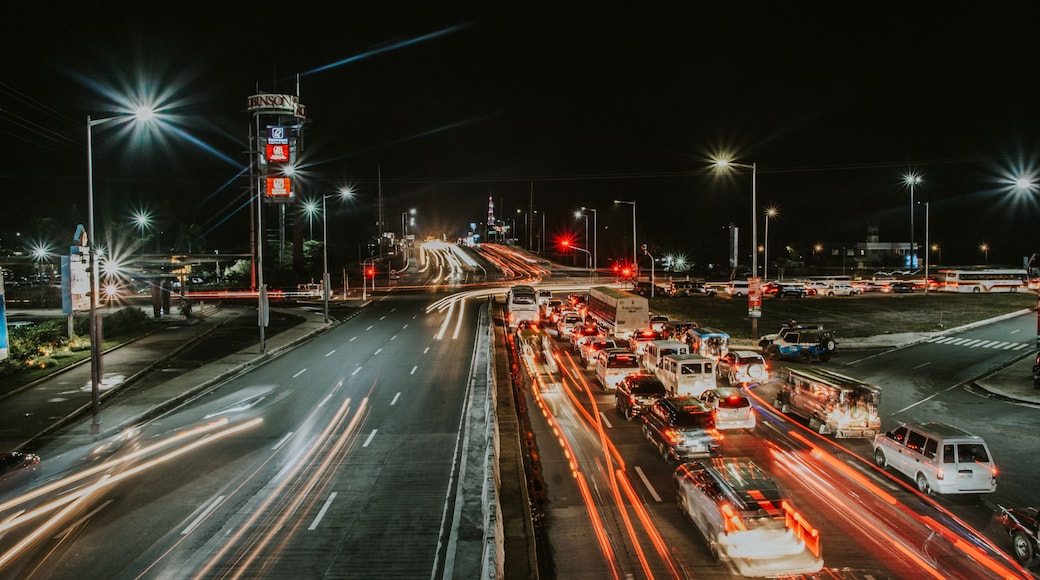 A nighttime cityscape with a busy intersection, illuminated signs, and a prominent tower.