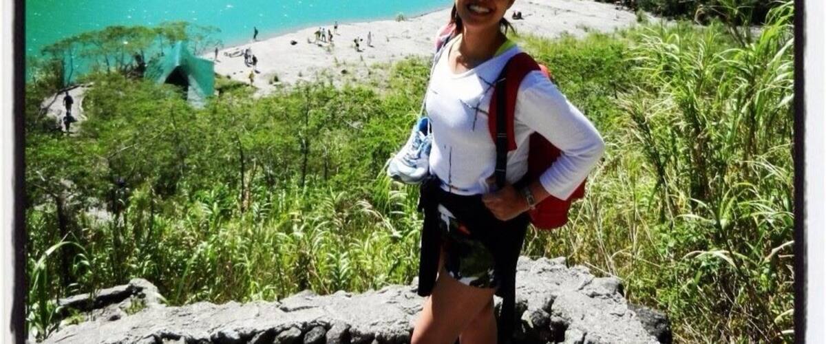 A person standing on a rocky outcrop overlooking a turquoise lake with mountains in the background.