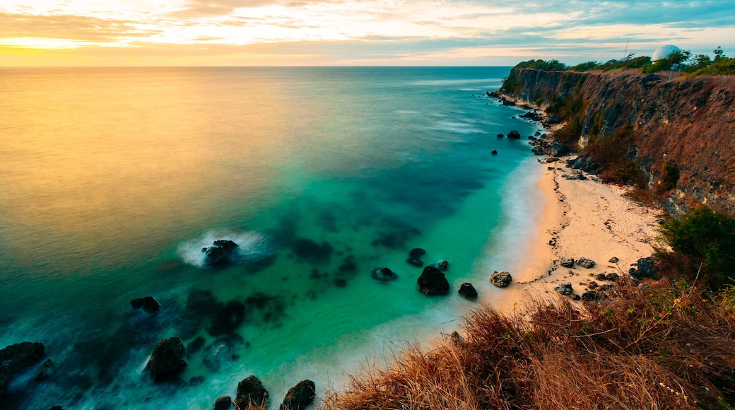 A coastal landscape with clear turquoise waters, a sandy beach, and rocky cliffs.