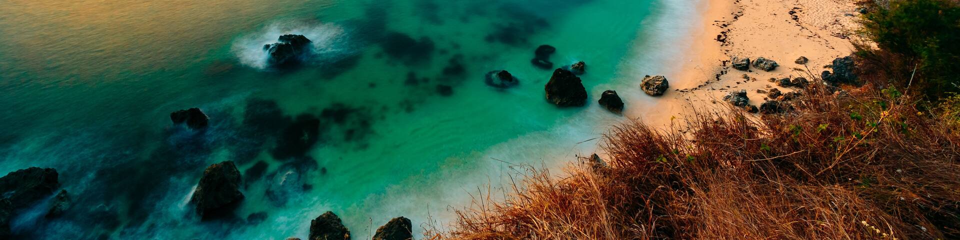 A coastal landscape with clear turquoise waters, a sandy beach, and rocky cliffs.