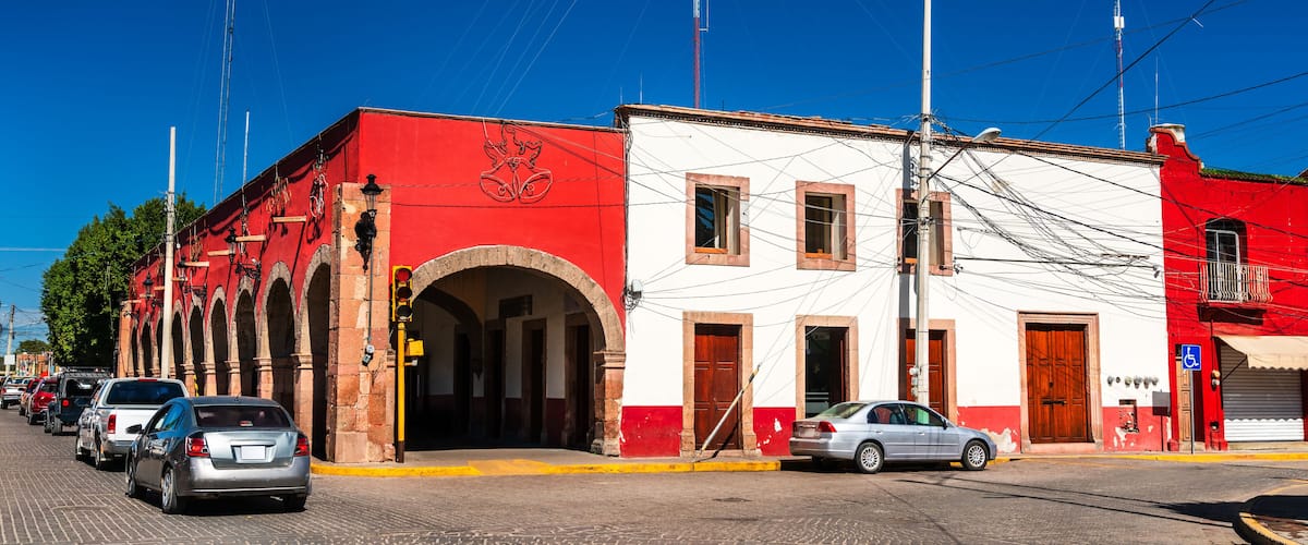 A street with red and white buildings, a clear blue sky, and a few parked cars.