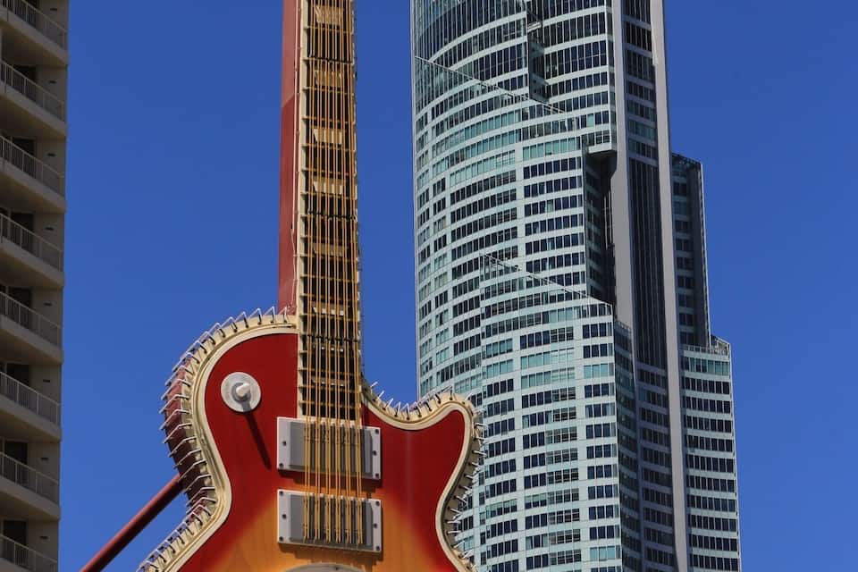 A Hard Rock Cafe sign with a guitar design, set against a city skyline.