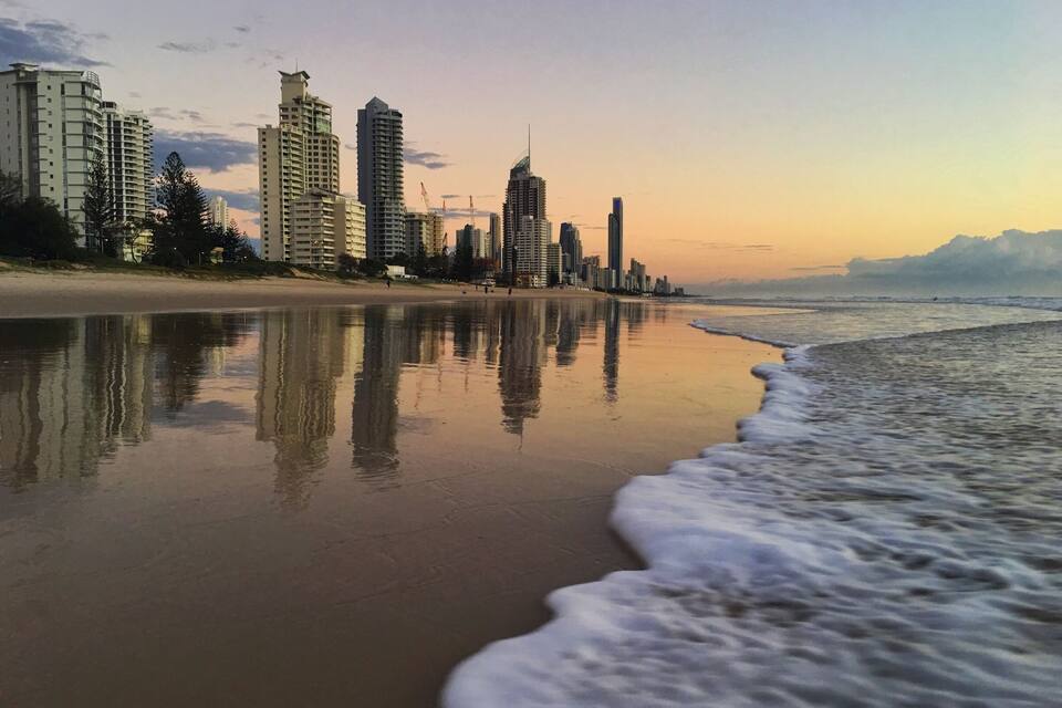 Una playa con un mar tranquilo que refleja edificios y árboles.