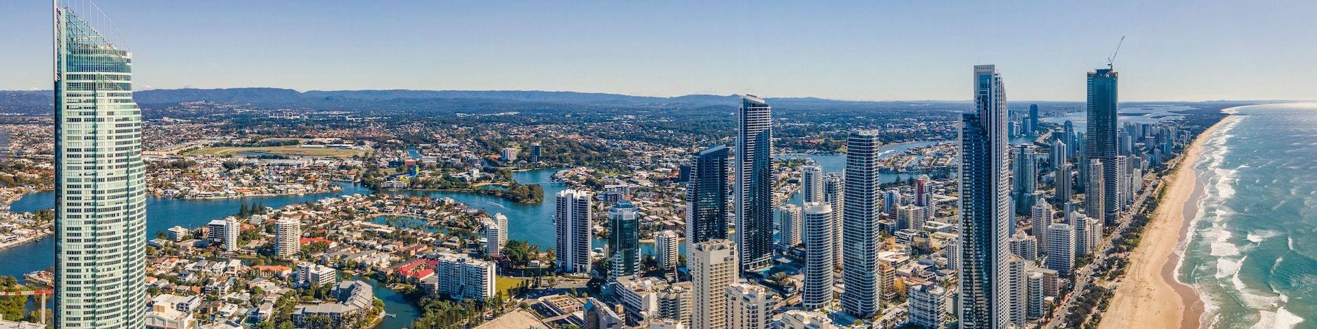 A coastal cityscape with high-rise buildings, a beach, and a marina.