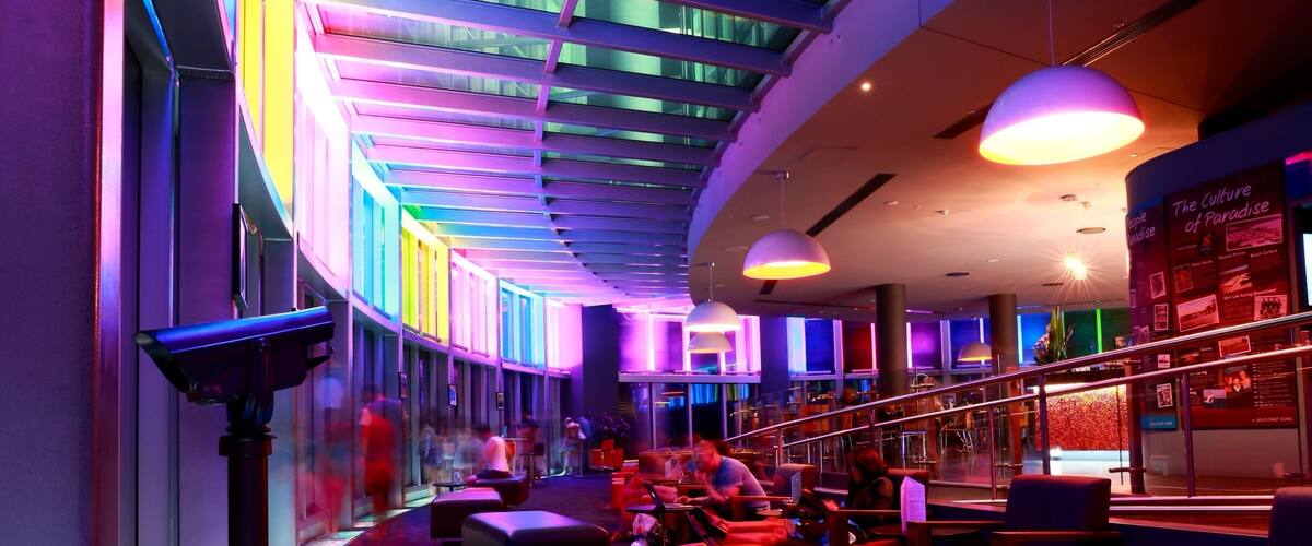 A modern indoor space with vibrant neon lighting, red seating, and a curved ceiling structure.