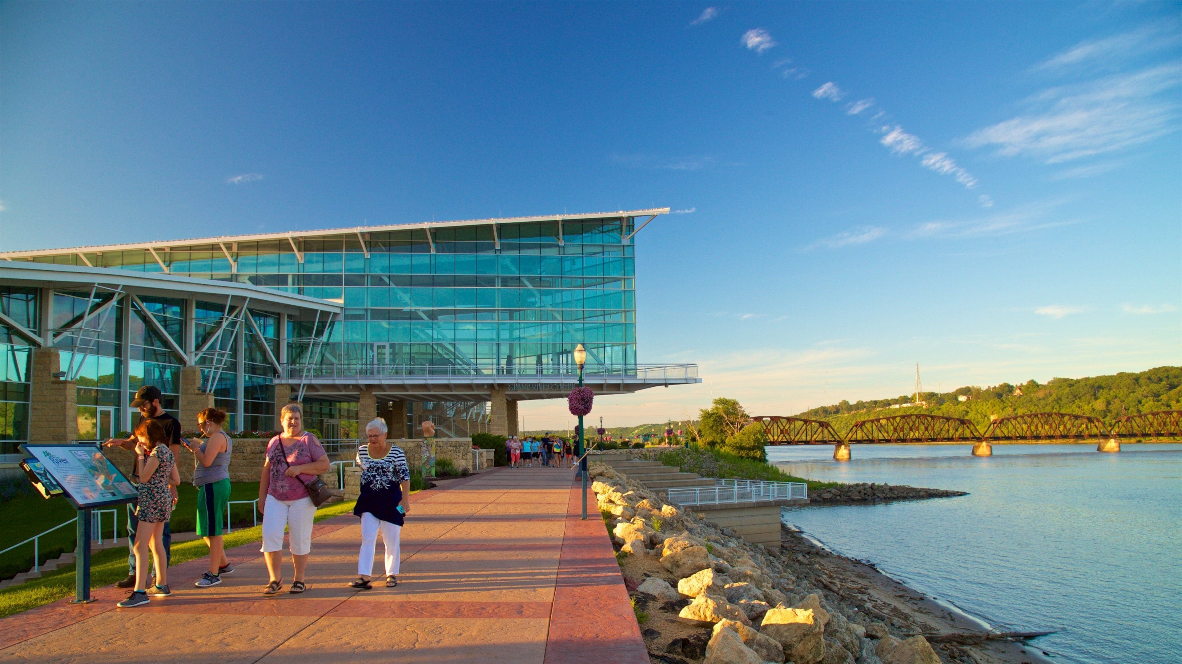 A modern glass building with a walkway leading to a river.