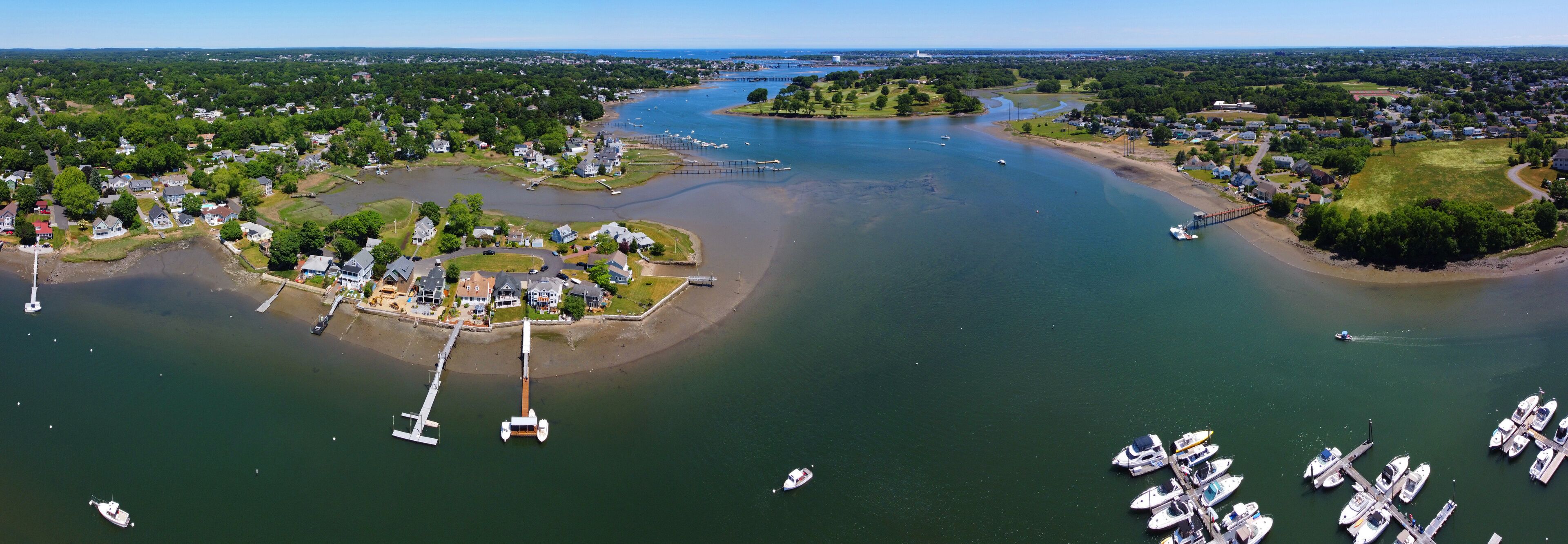 An aerial view of a coastal town with a marina, boats, and a bridge connecting to an island.