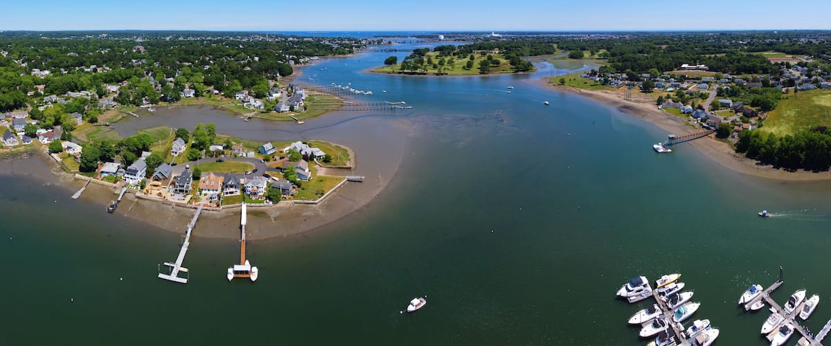 An aerial view of a coastal town with a marina, boats, and a bridge connecting to an island.