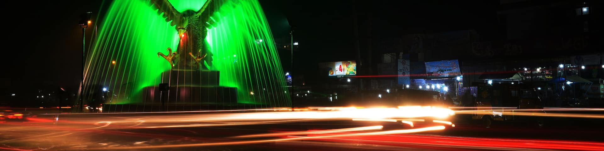Light trails of vehicles and traffic around an illuminated monument of Sargodha with a showering fountain. It's a long exposure shoot of 30 seconds with selective focus.