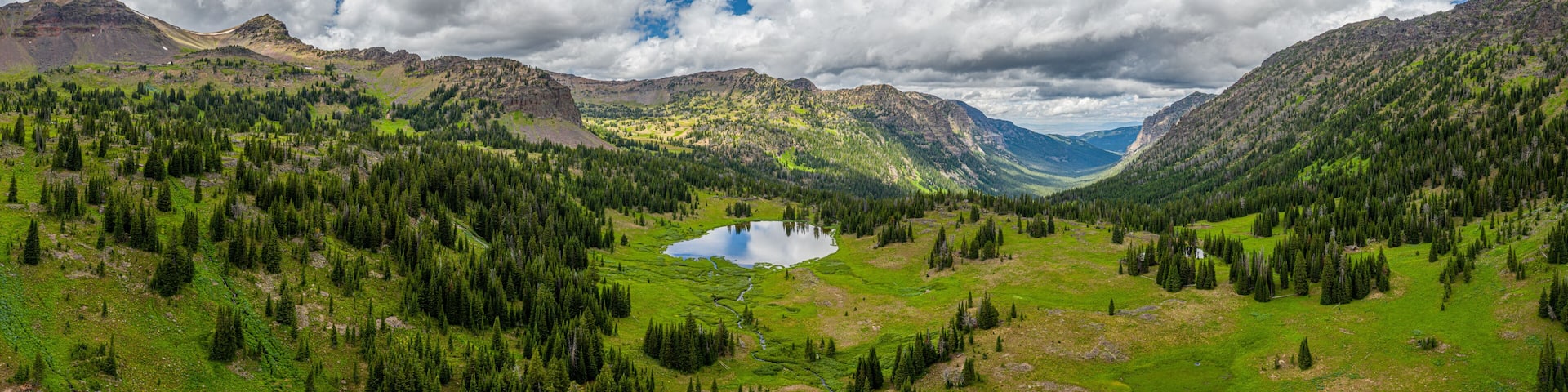 A mountainous landscape with a lake surrounded by dense forests and rugged terrain.