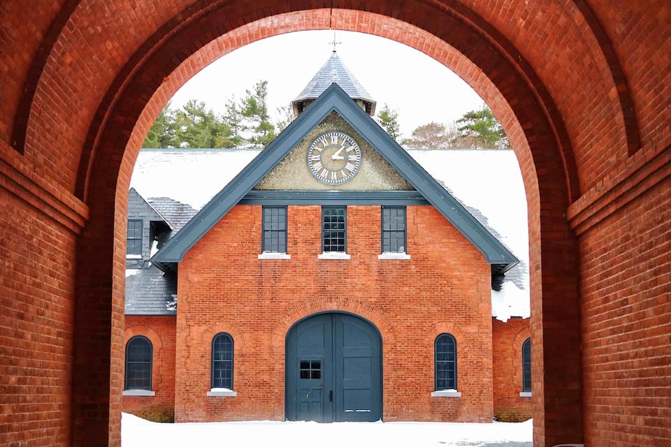 A red brick building with a clock tower, arched brick structures, and a snow-covered ground.
