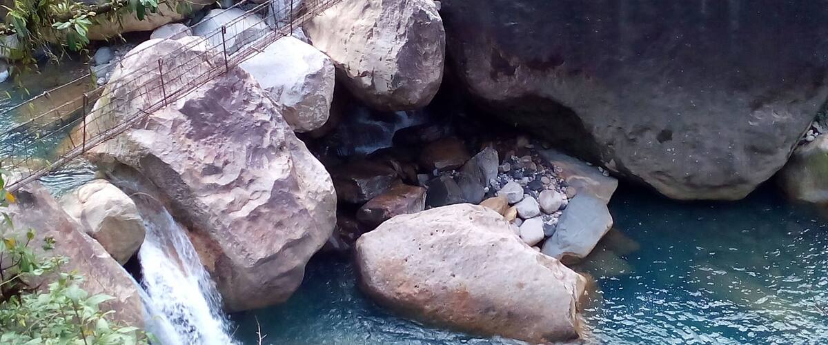 A waterfall cascading over rocks into a clear pool surrounded by large boulders and greenery.