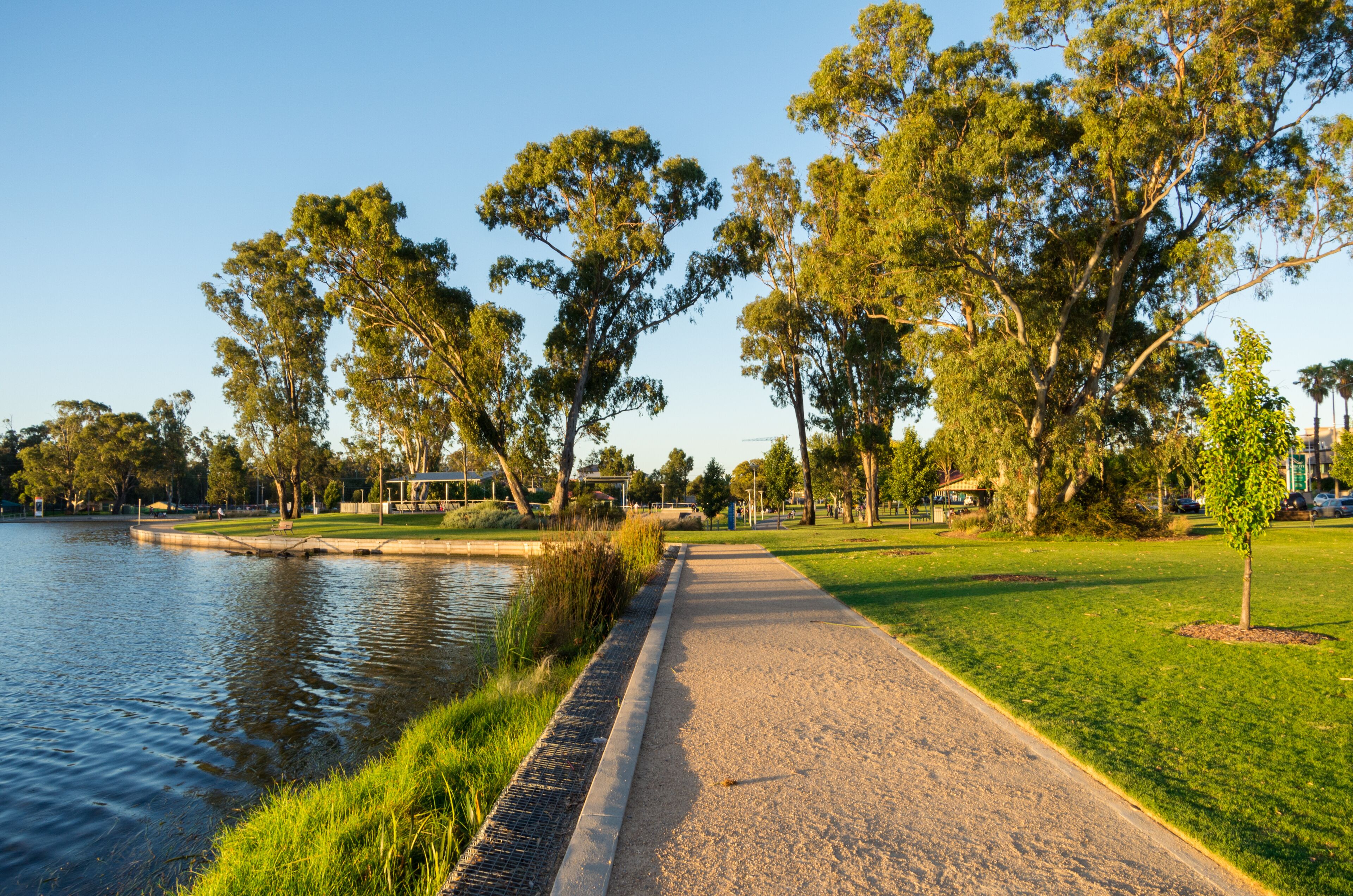 A riverside walkway with a gravel path, grassy areas, and trees.