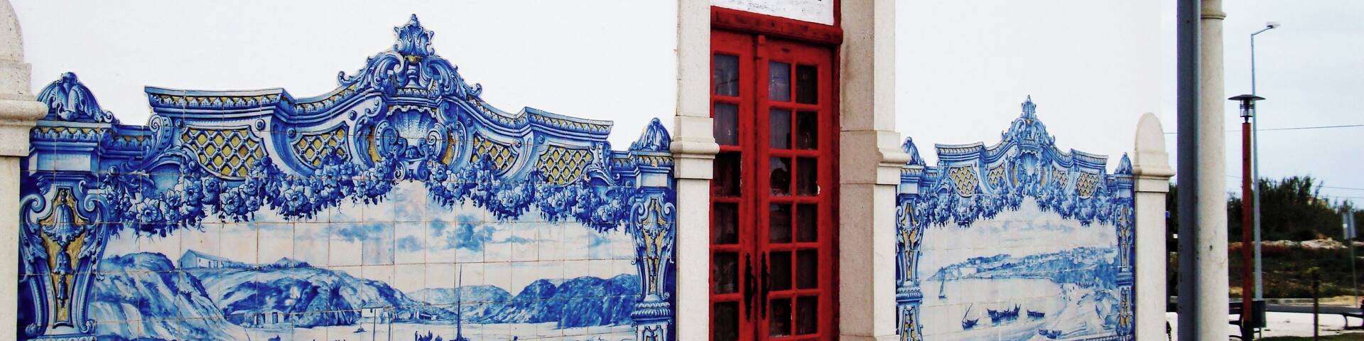 A building with a red door and blue and white tiles depicting a coastal scene.