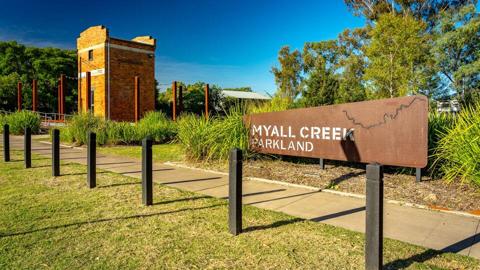 A sign for Myall Creek Parkland with a brick structure in the background.