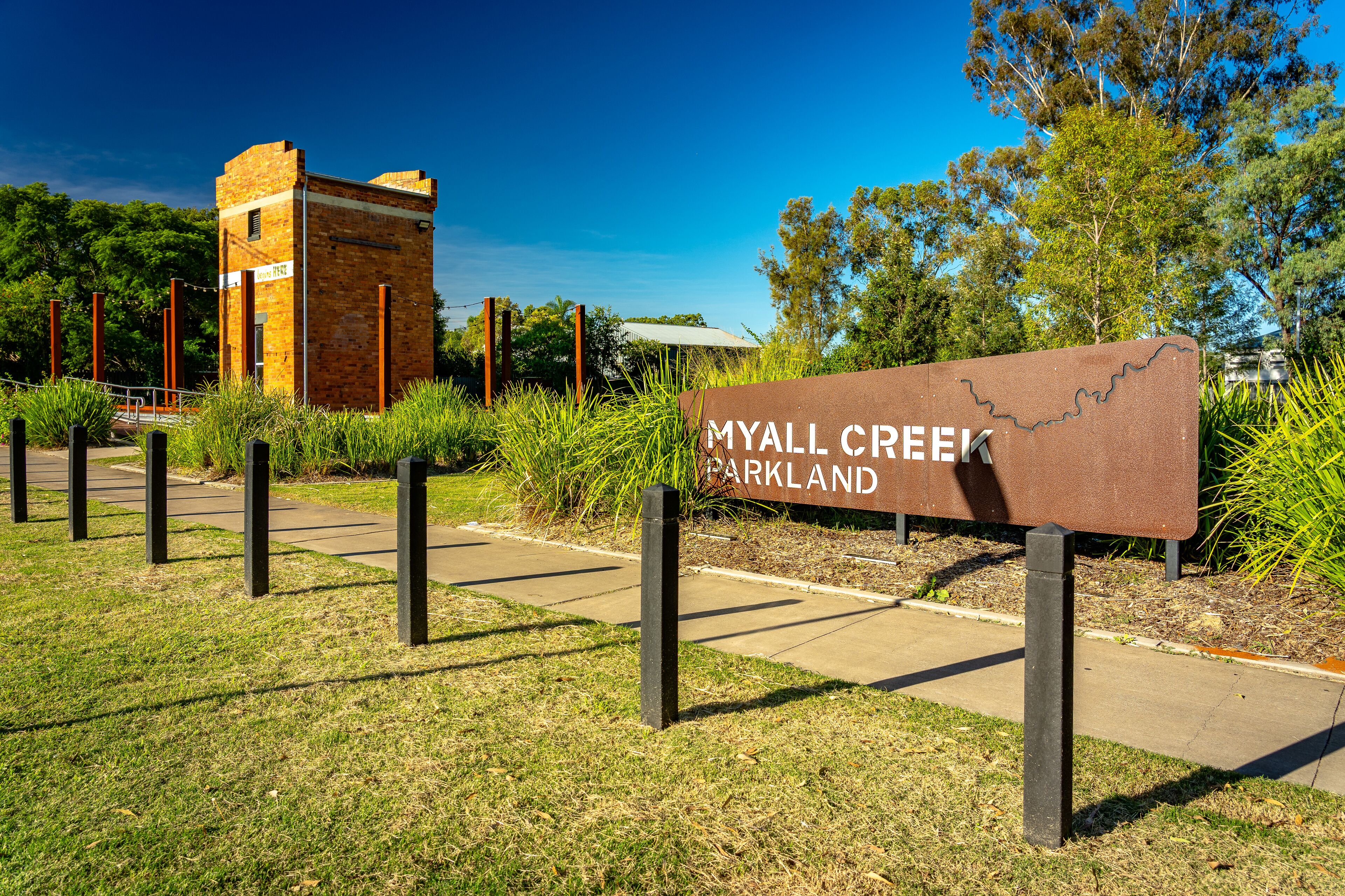 A sign for Myall Creek Parkland with a brick structure in the background.