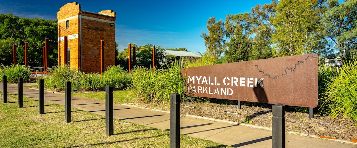 A sign for Myall Creek Parkland with a brick structure in the background.