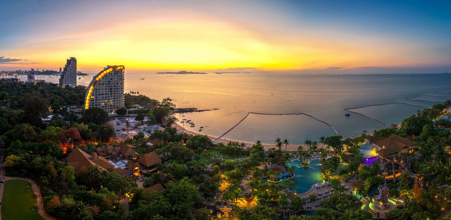 Un resort costero con una piscina grande, palmeras y un atardecer sobre el agua.