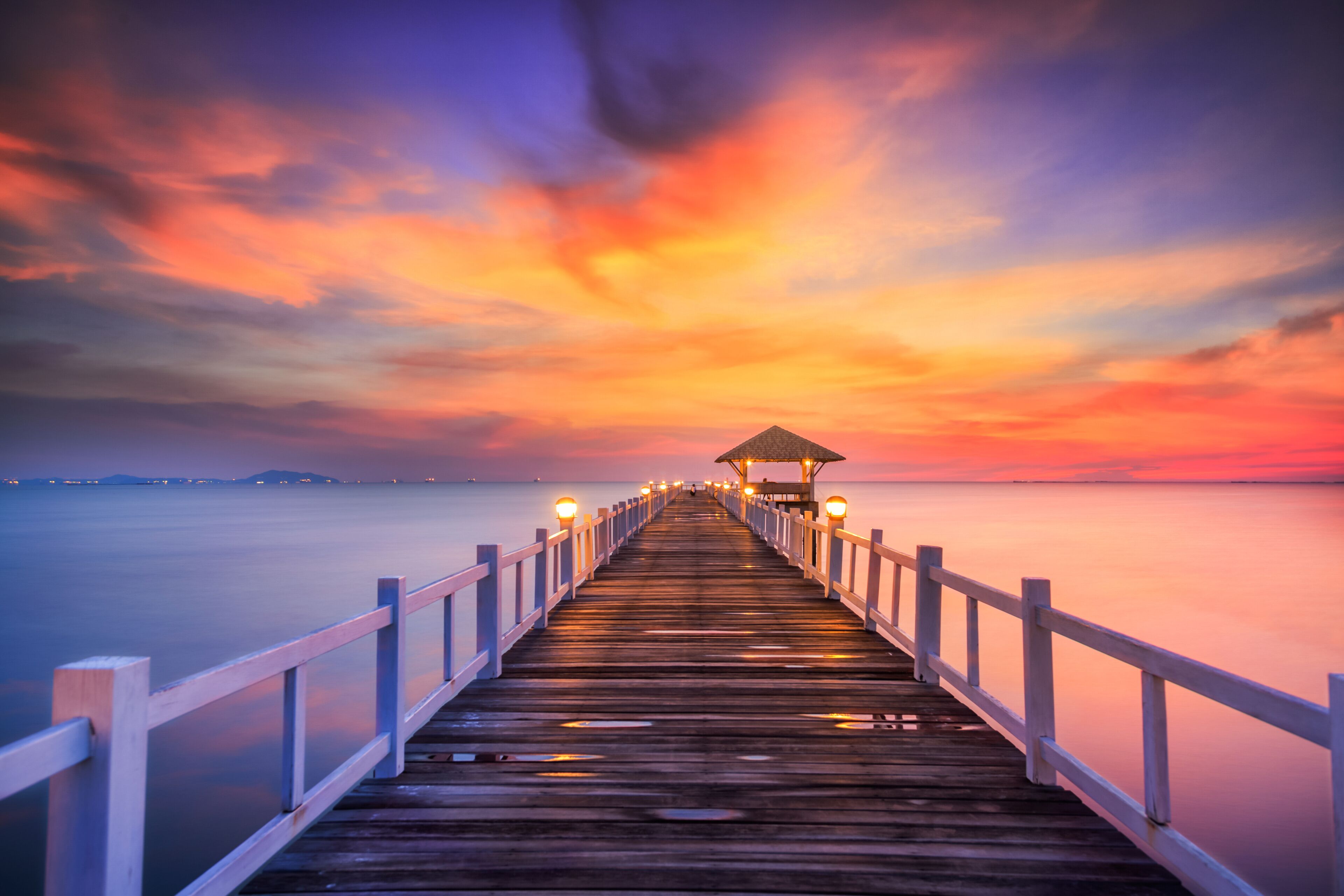 A wooden pier extending into calm waters at sunset with a gazebo at the end.