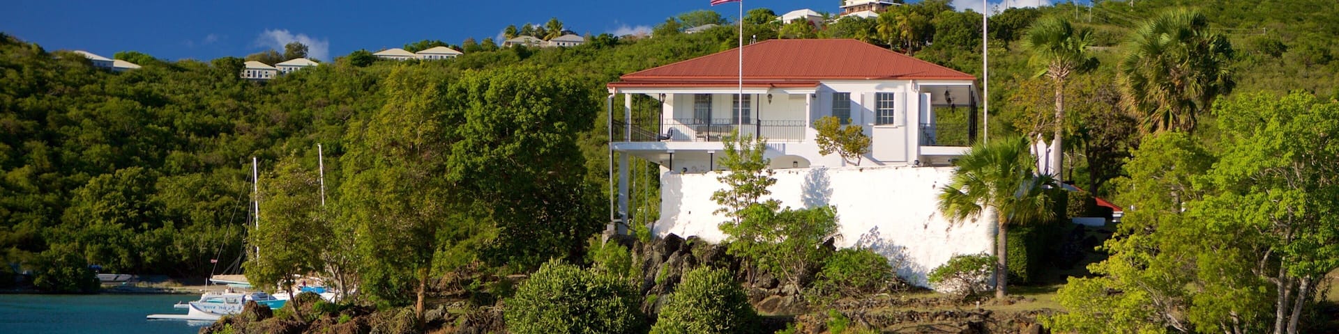 A white house with a red roof on a hillside overlooking turquoise waters.