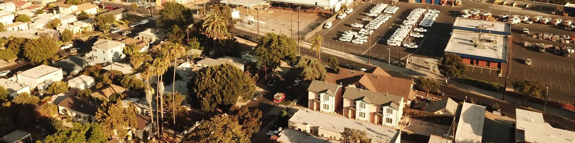 Aerial view of South Los Angeles with residential neighborhoods, commercial buildings, parking lots, and palm trees under warm golden hour light in Los Angeles, California, United States.
