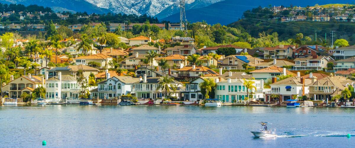 A coastal town with houses, boats, and snow-capped mountains in the background.