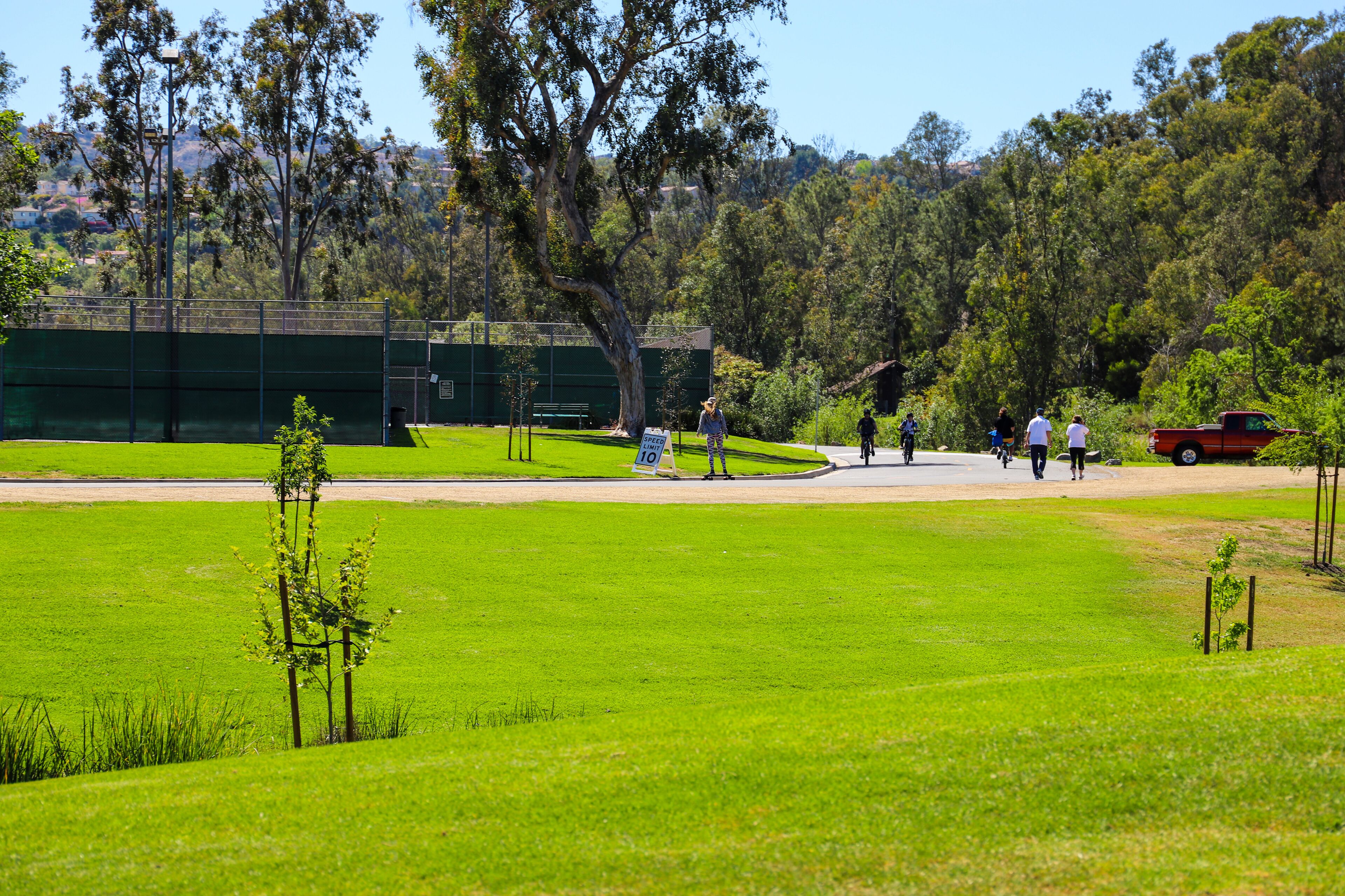 people walking, riding bikes and electric skateboards in the park with lush green grass and trees and blue sky  at Laguna Niguel Regional Park in Laguna Niguel, California