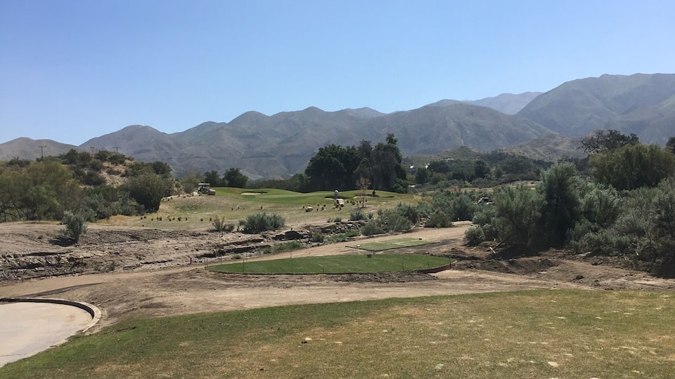 A golf course with a clear sky, green grass, and distant mountains.