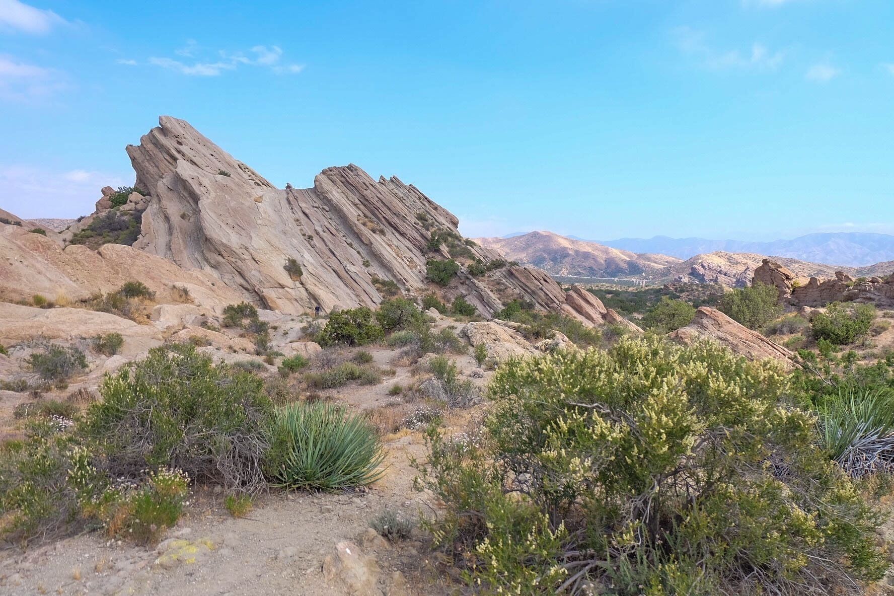 A rocky desert landscape with prominent sandstone formations and sparse vegetation.