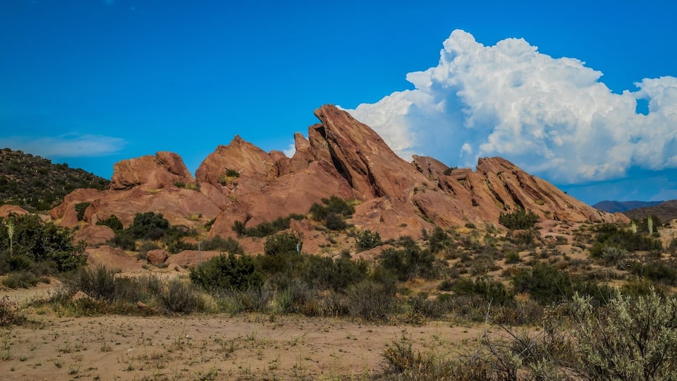 A desert landscape with prominent red rock formations and sparse vegetation under a clear blue sky.