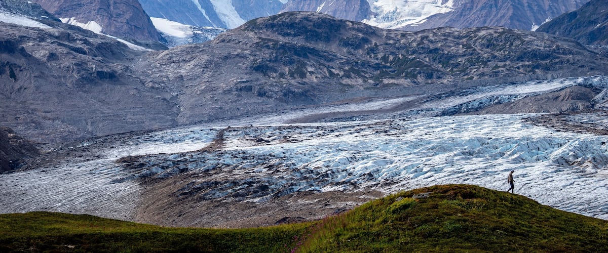 A glacier in a mountainous region with snow-capped peaks in the background.
