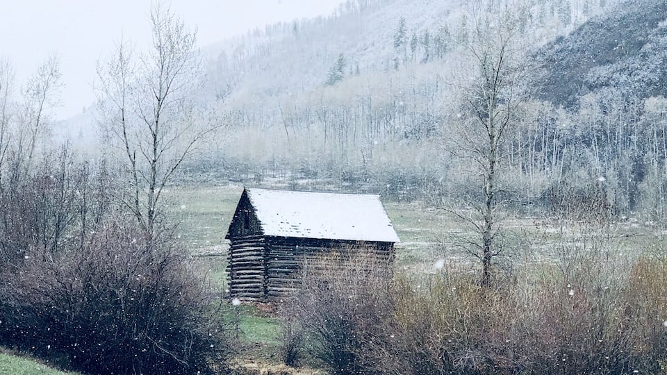 A wooden cabin in a snowy landscape with a river in the foreground.