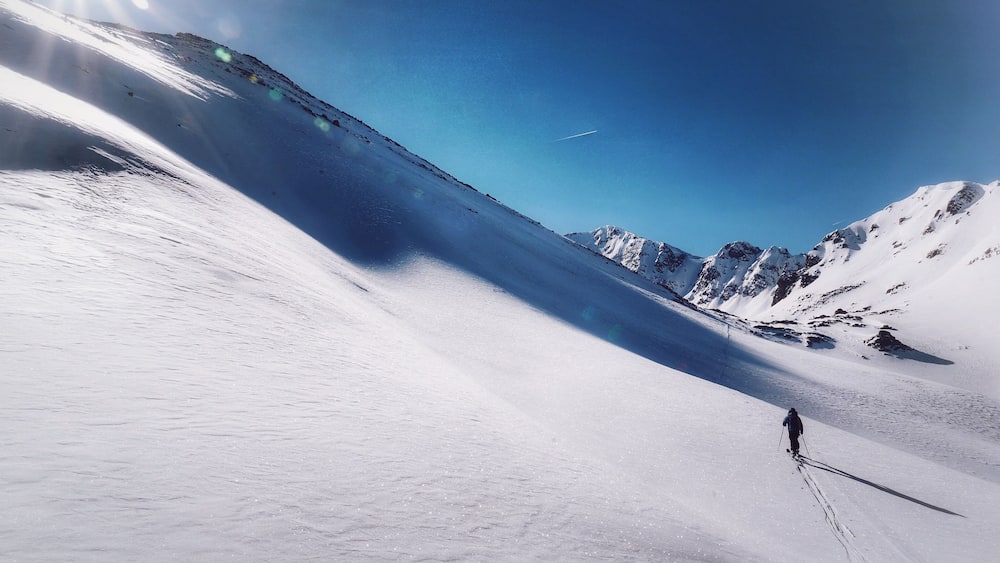 A skier descending a snow-covered slope with a clear blue sky and distant mountains.