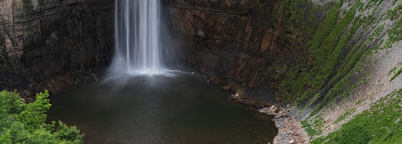 A waterfall cascading down a rocky cliff into a calm pool surrounded by lush greenery.