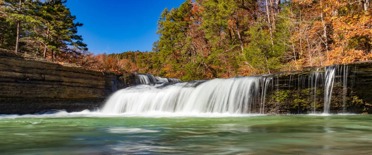 A waterfall in a forested area with autumn foliage.