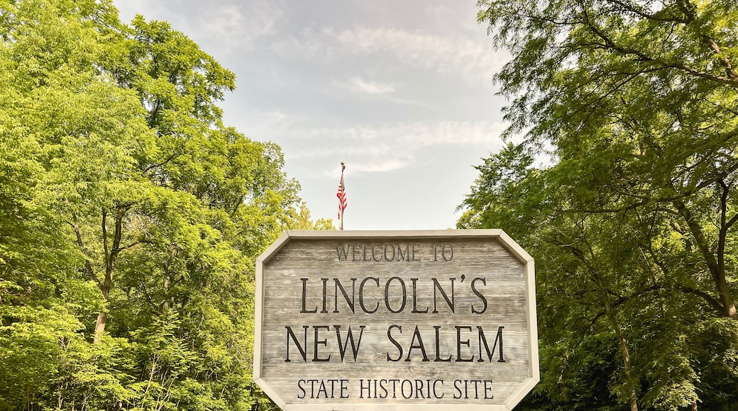 A wooden welcome sign for Lincoln's New Salem State Historic Site surrounded by lush greenery and a clear sky.