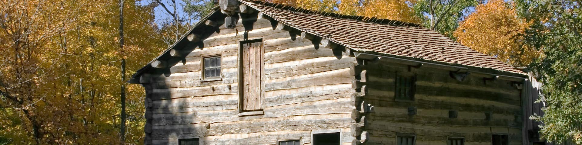 A rustic log cabin with a wooden staircase and a wooden fence in the background.
