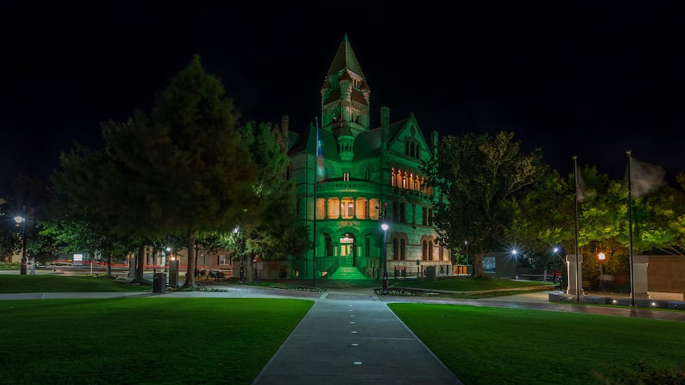 A green-lit Victorian-style building with a prominent tower, a well-maintained lawn, and a clear pathway leading to the entrance.