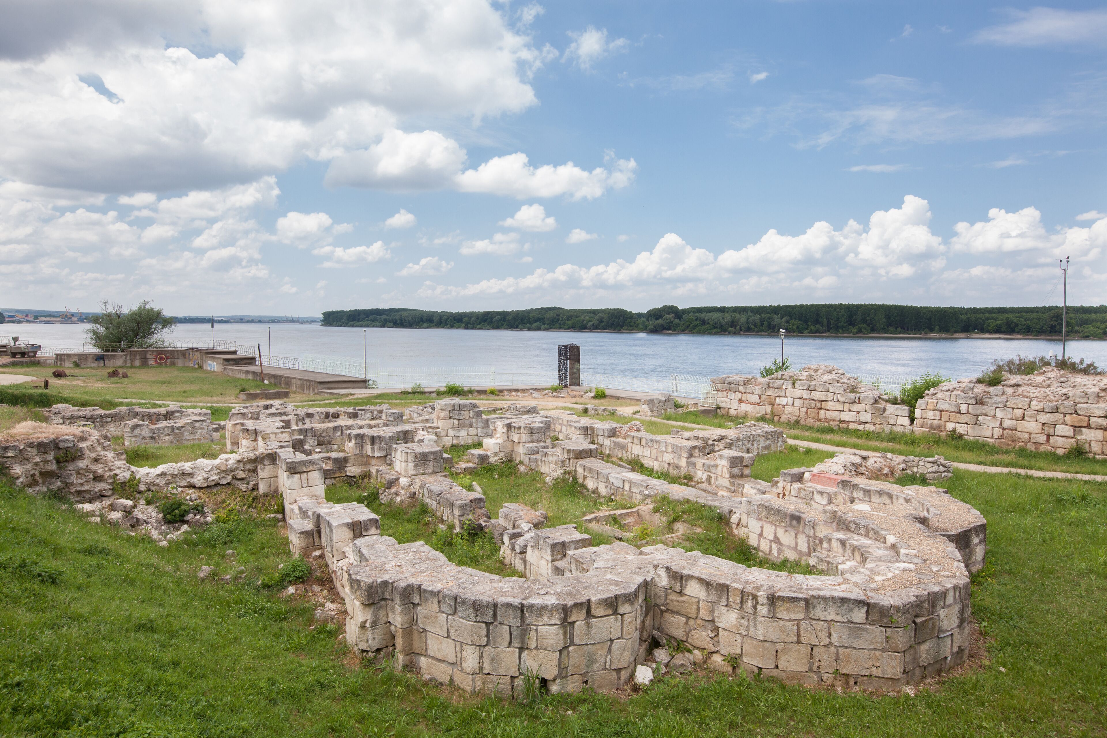Ancient stone ruins by a lake with a clear sky.