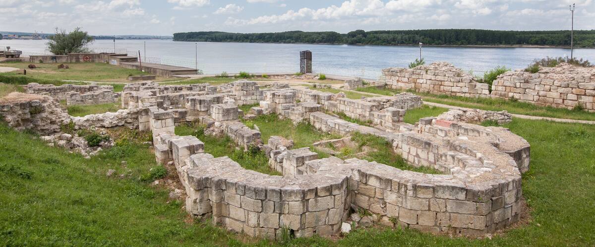 Ancient stone ruins by a lake with a clear sky.