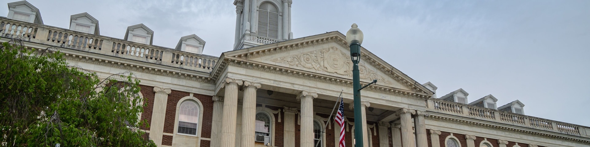 Un grand bâtiment historique, remarquable par son imposante tour de l’horloge, ses colonnes et son drapeau.