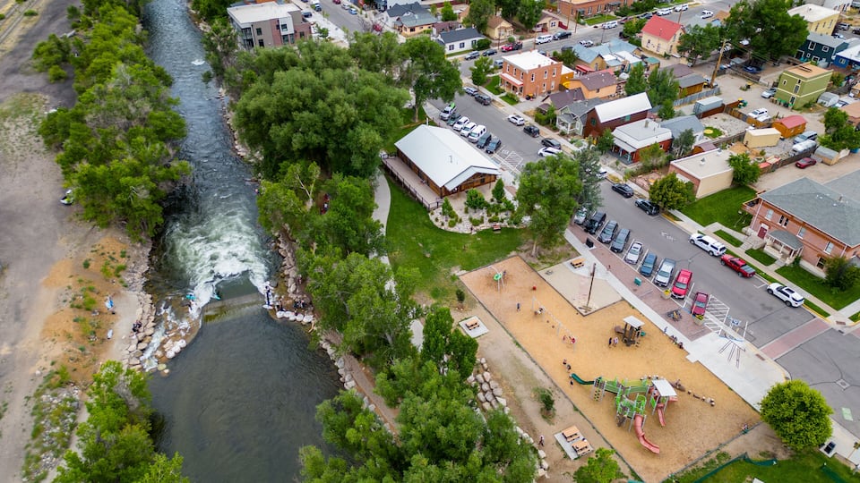 An aerial view of a riverside town with a playground and a large building with a red roof.