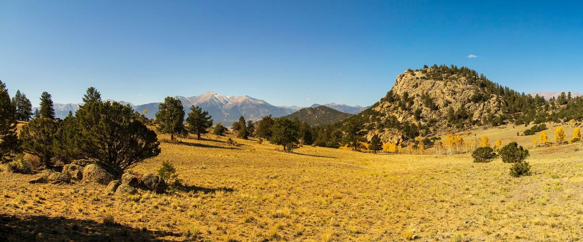 A mountainous landscape with a clear sky, sparse vegetation, and a prominent rocky hill.