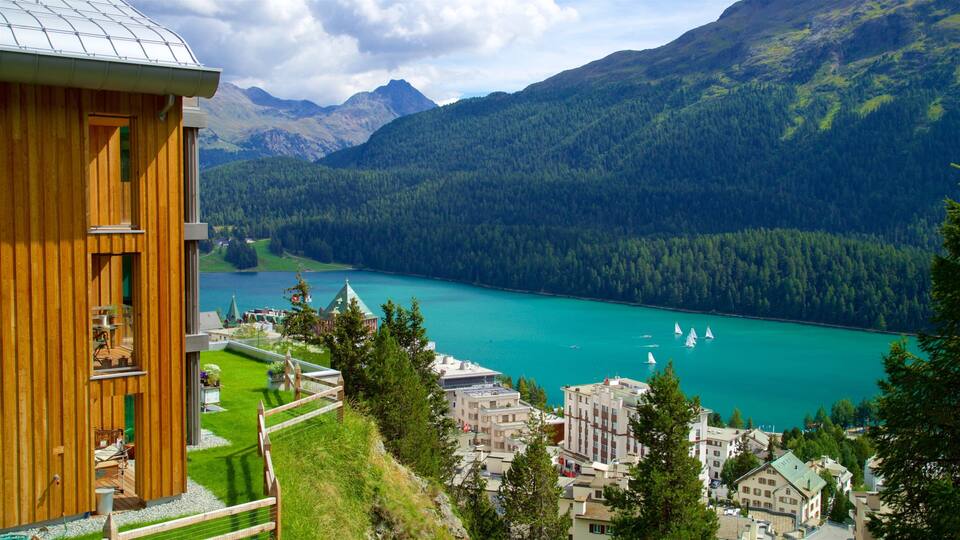 A wooden building overlooking a turquoise lake with sailboats, surrounded by forested mountains.