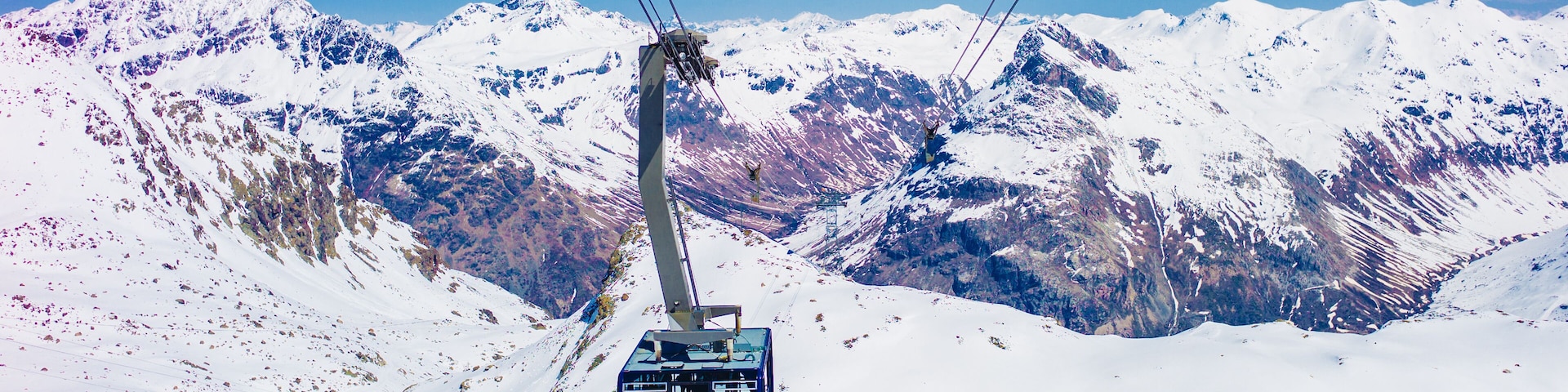 A cable car ascending a snowy mountain with a clear sky.