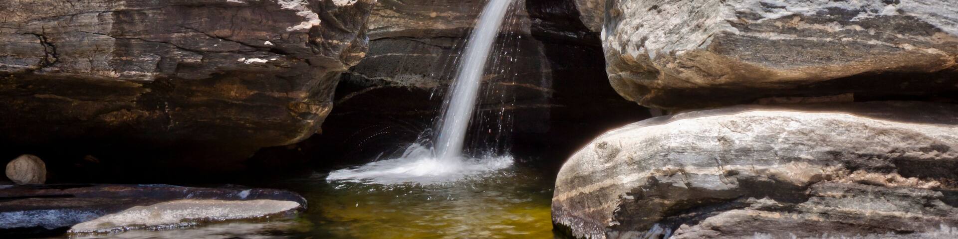 A waterfall cascading down a rocky gorge with large boulders surrounding the water.