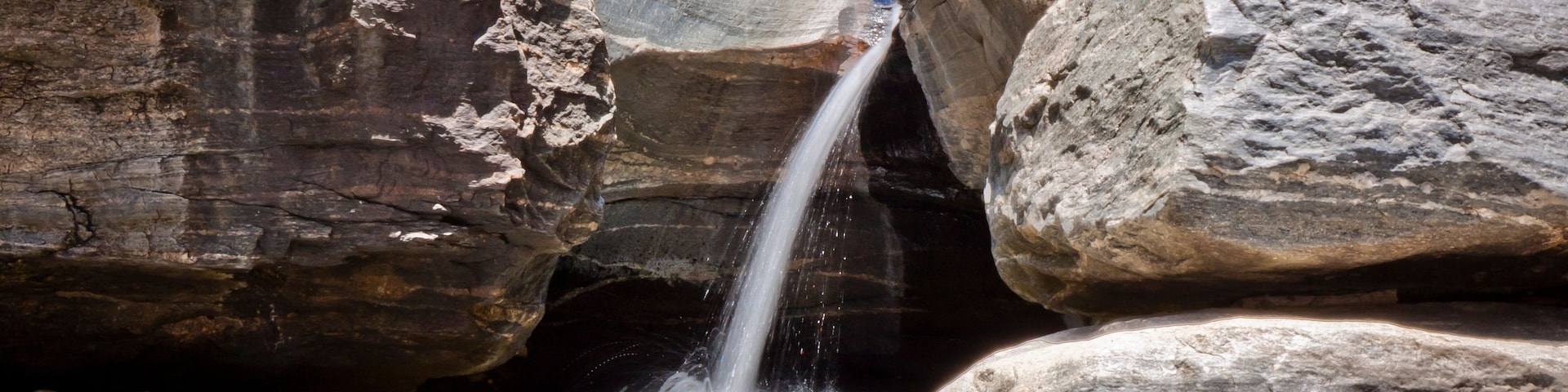 Una cascada se precipita por un desfiladero rocoso, con grandes rocas alrededor del agua.