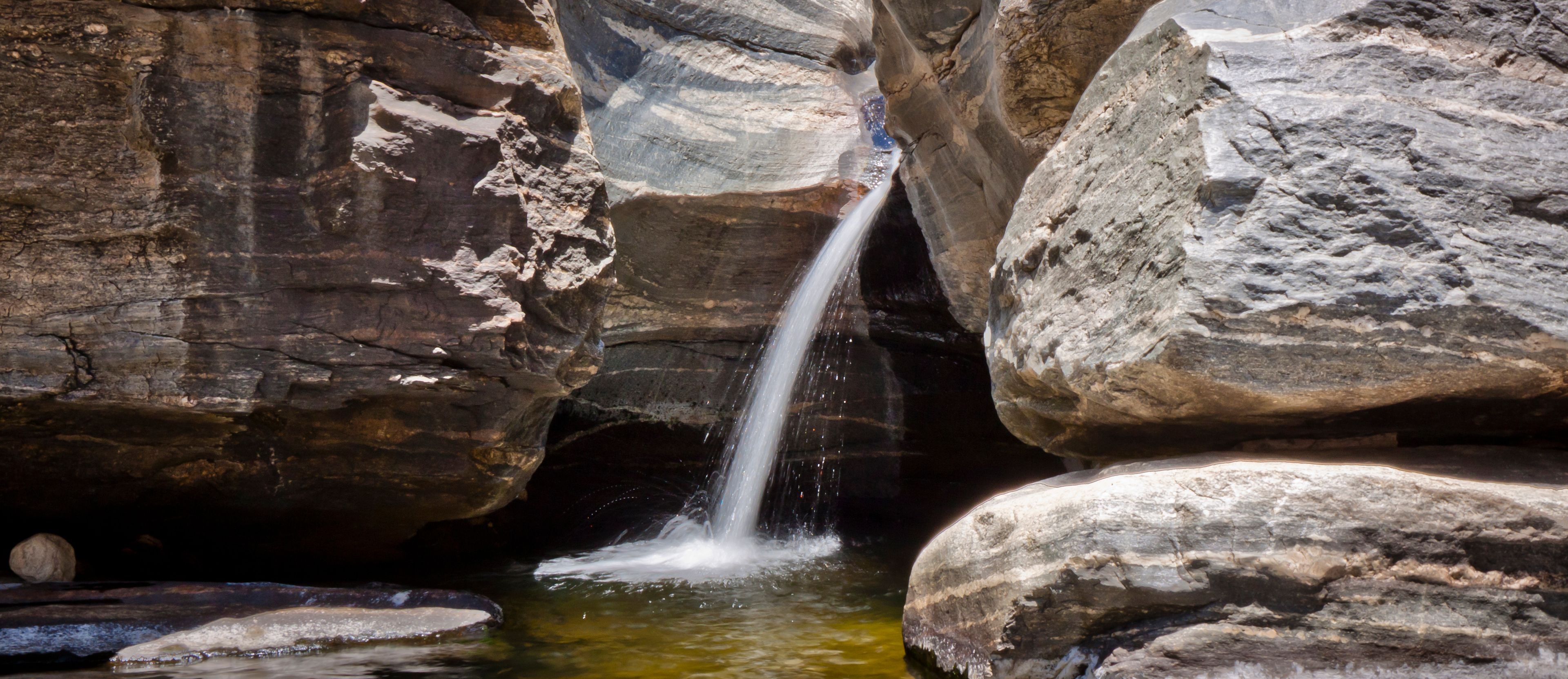 A waterfall cascading down a rocky gorge with large boulders surrounding the water.